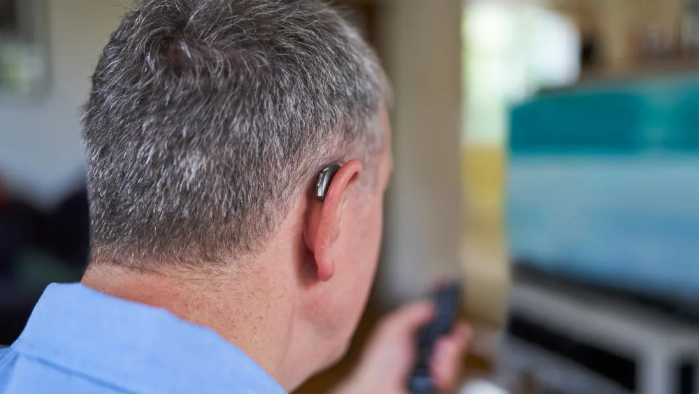 Mature man wearing a wireless hearing aid at home