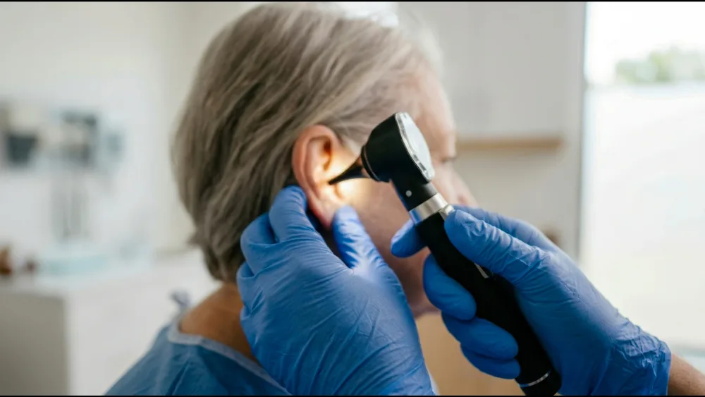 Audiologist examining an elderly patient's ear with an otoscope during a home visit
