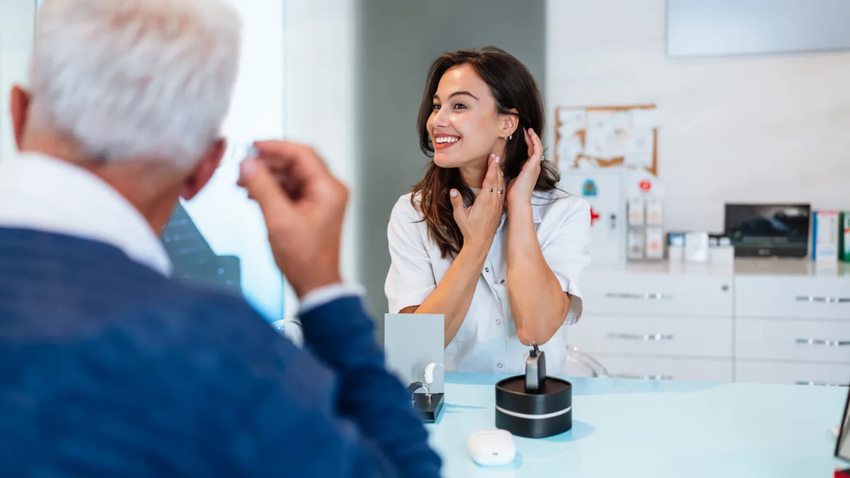 Audiologist showing a patient how a hearing aid sits behind the ear